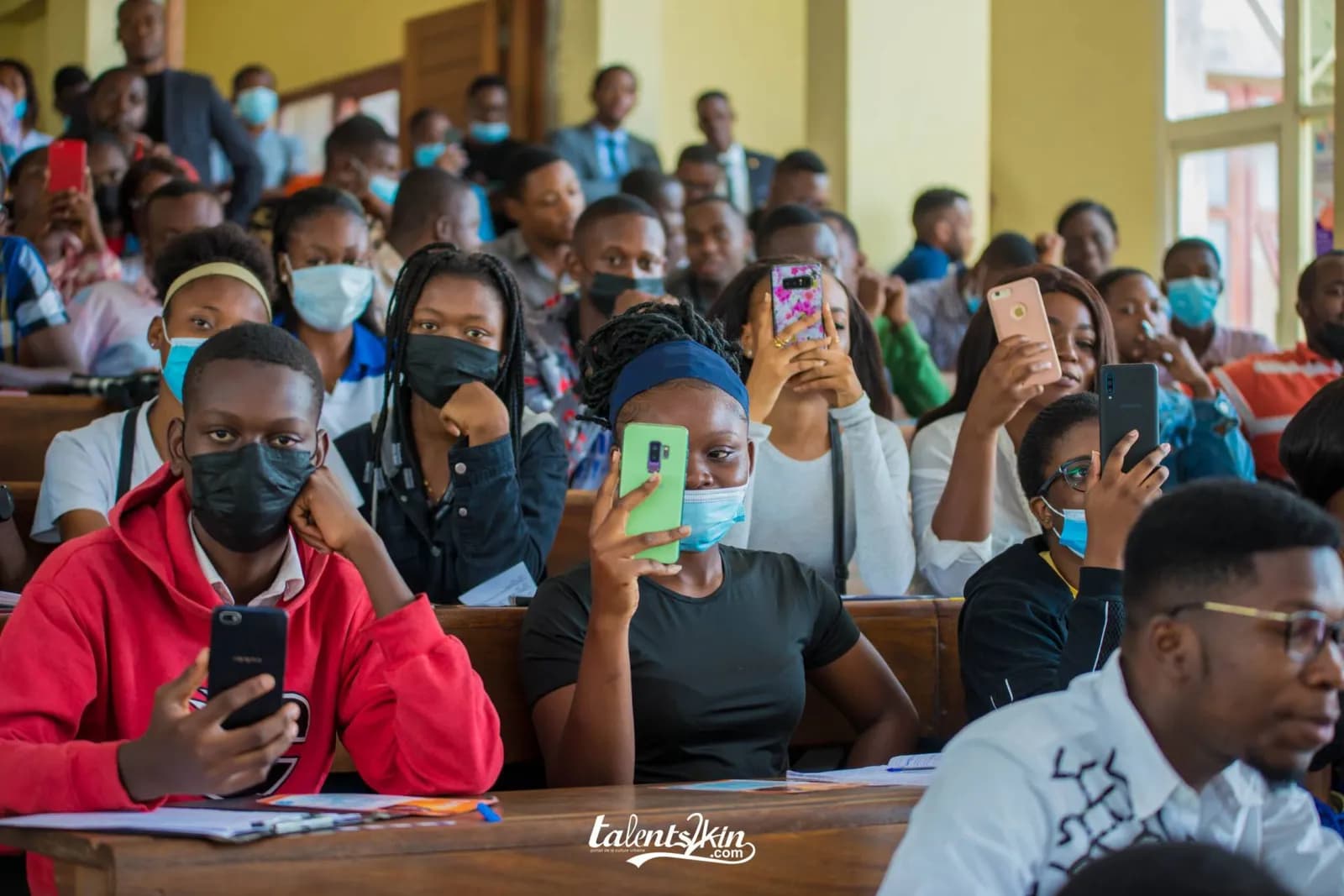 Des étudiants assis sur les bancs d'un amphithéâtre suivent une conférence, plusieurs filment la présentation avec leur téléphone.